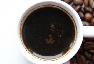 כוס קפה על רקע לבן עם פולי קפה שמסמל חוקן קפה שמאוד תורם לבריאות