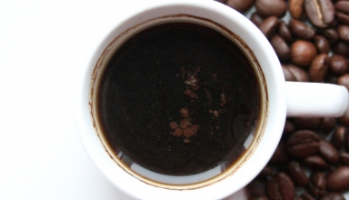 כוס קפה על רקע לבן עם פולי קפה שמסמל חוקן קפה שמאוד תורם לבריאות