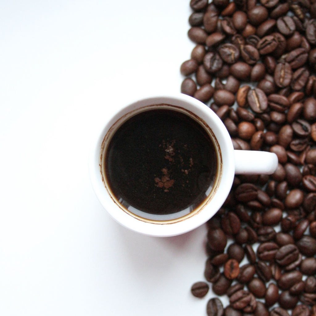 כוס קפה על רקע לבן עם פולי קפה שמסמל חוקן קפה