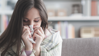 אישה שמקנחת את האף וסובלת משפעת שייתכן ויותר מסוכנת השנה